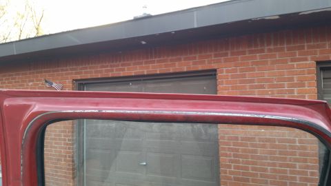 1981 Ford Bronco - Close-up of a red vehicle's door frame, showing the weatherstripping and a small American flag mounted near a garage door.