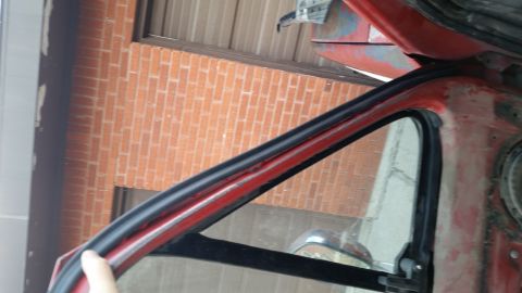 1981 Ford Bronco - A close-up view of the weatherstripping around a car door frame, with a brick wall visible behind it.