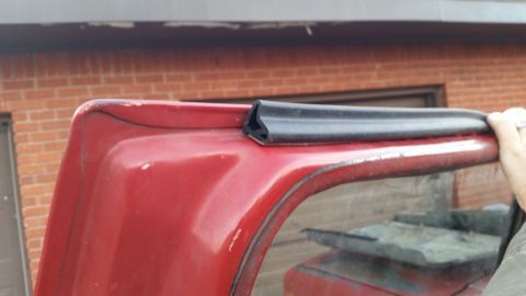 1981 Ford Bronco - Close-up of weatherstripping on a red vehicle's roofline, with a brick building in the background.