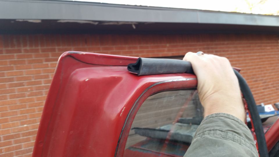 Red vehicle's top edge with weatherstripping being held by a hand