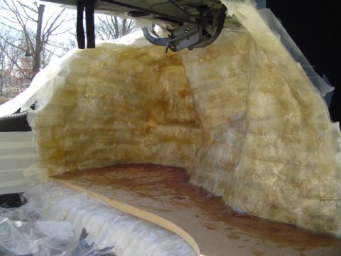1999 Ford Taurus - Wide view inside an open trunk shell with resin-soaked fiberglass mat covering the full rear bulkhead and both quarter panels, resin runnin…