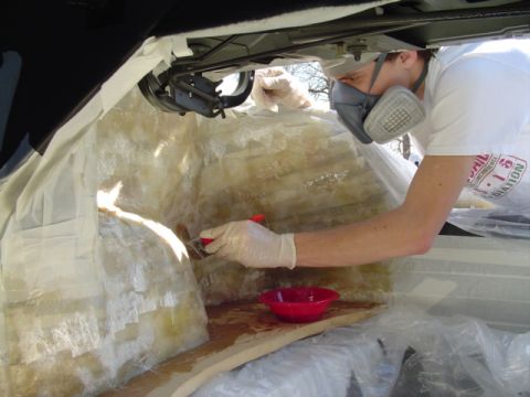 1999 Ford Taurus - A person in a white shirt, respirator and latex gloves brushes resin over fiberglass matting laid into a masked-off car trunk, building a c…