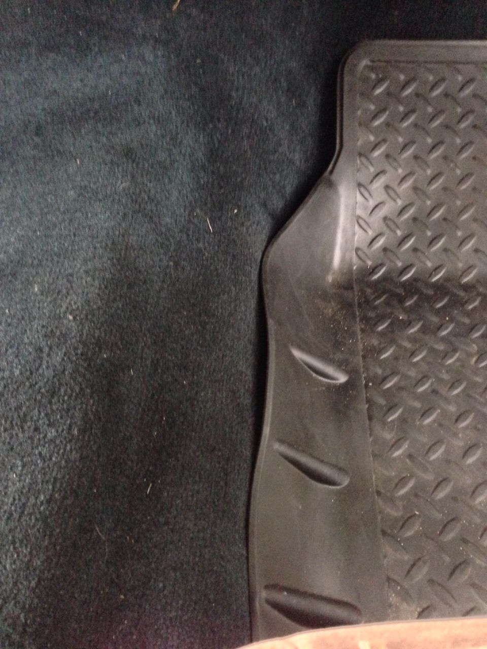 Close-up of a black rubber floor mat with diamond tread pattern on dark carpet