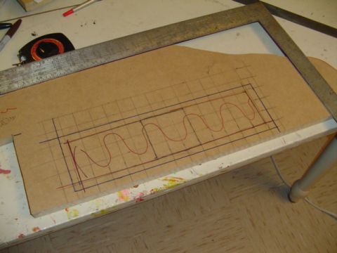 1999 Ford Taurus - Cardboard template on a paint-spattered workbench marked with a pencil grid and red serpentine curves, with a metal framing square and a ta…
