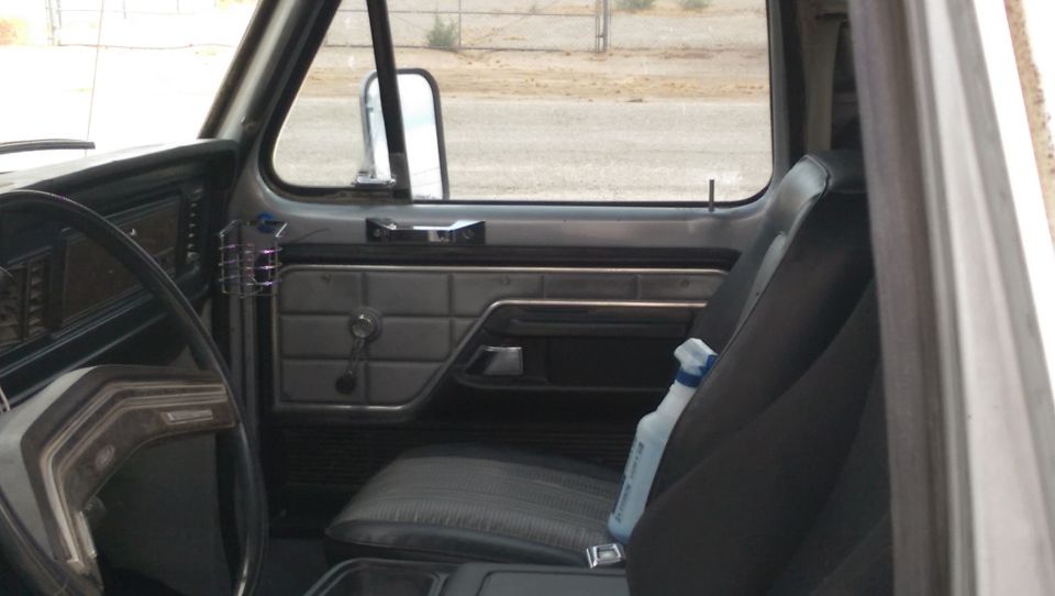 1978 Ford Bronco interior showing dashboard, door panel, and seats. A spray bottle is on the passenger seat