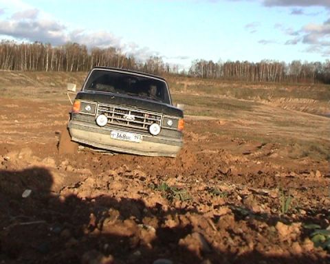1987 Ford Bronco - A black 1987 Ford Bronco is stuck in the mud on a dirt track, with trees in the background.