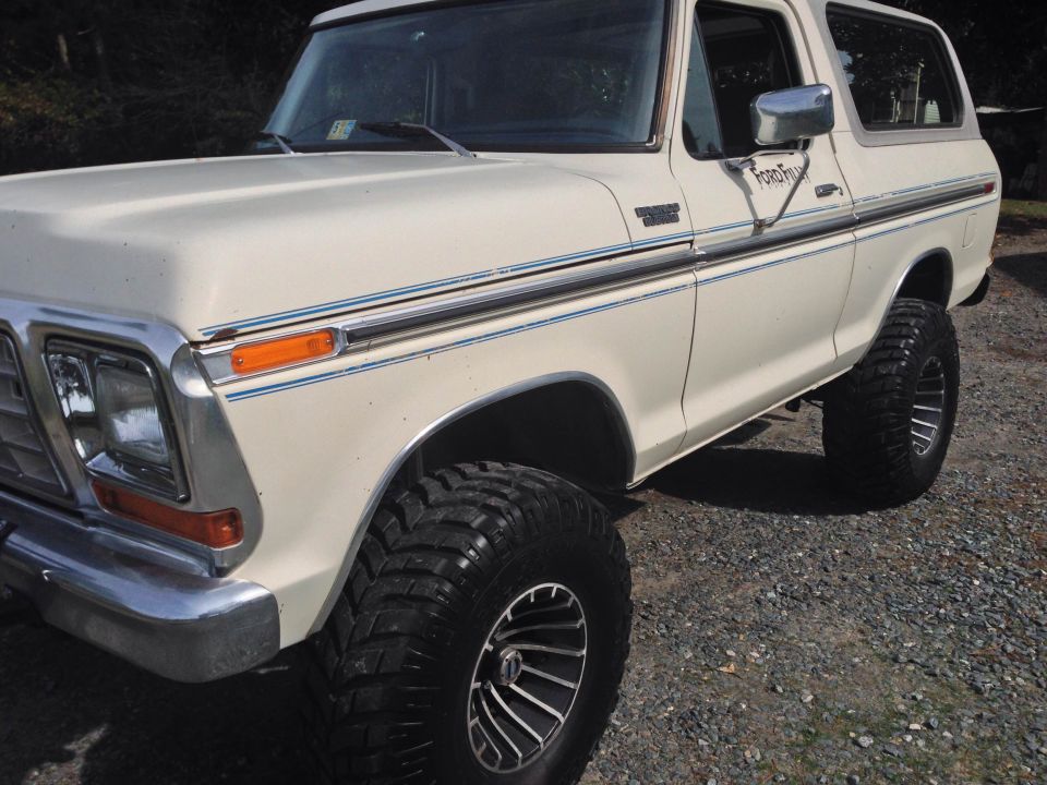 White Ford Bronco with aftermarket wheels and tires. Side view shows chrome trim and Ford Bronco badging