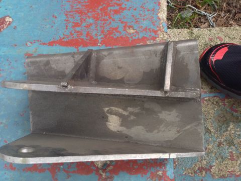 1979 Ford Bronco - A metal bracket is shown resting on a weathered surface, with a shoe visible in the upper right corner.