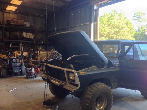 1979 Ford Bronco - A dark blue 1978 Ford Bronco sits in a cluttered garage with its hood raised, revealing the engine bay.