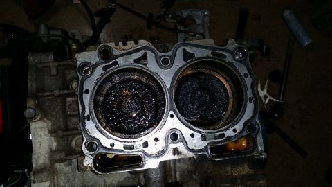 2007 Subaru Impreza - Close-up of an engine block showing two cylinders filled with carbon deposits and a damaged gasket.