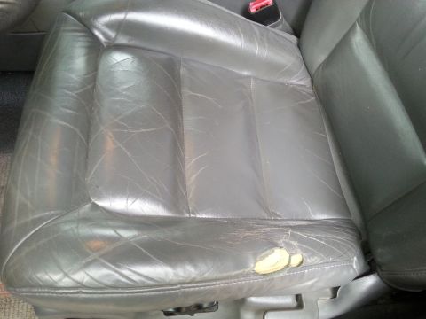 2001 Ford Explorer - The interior of a vehicle shows a damaged gray leather seat with a tear exposing yellow padding.