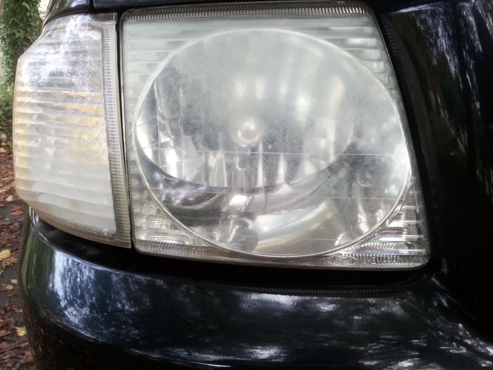 Close-up of a dusty headlight assembly on a dark vehicle