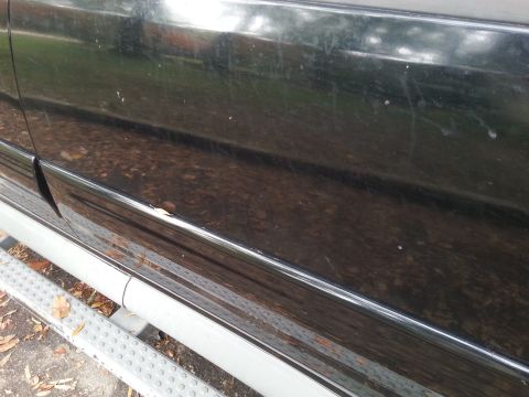 2001 Ford Explorer - Close-up of the lower side panel and running board of a black SUV, with some minor rust spots visible.