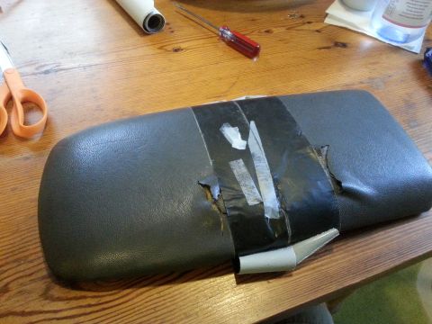 2001 Ford Explorer - A damaged center console armrest is taped up and sits on a wooden surface.