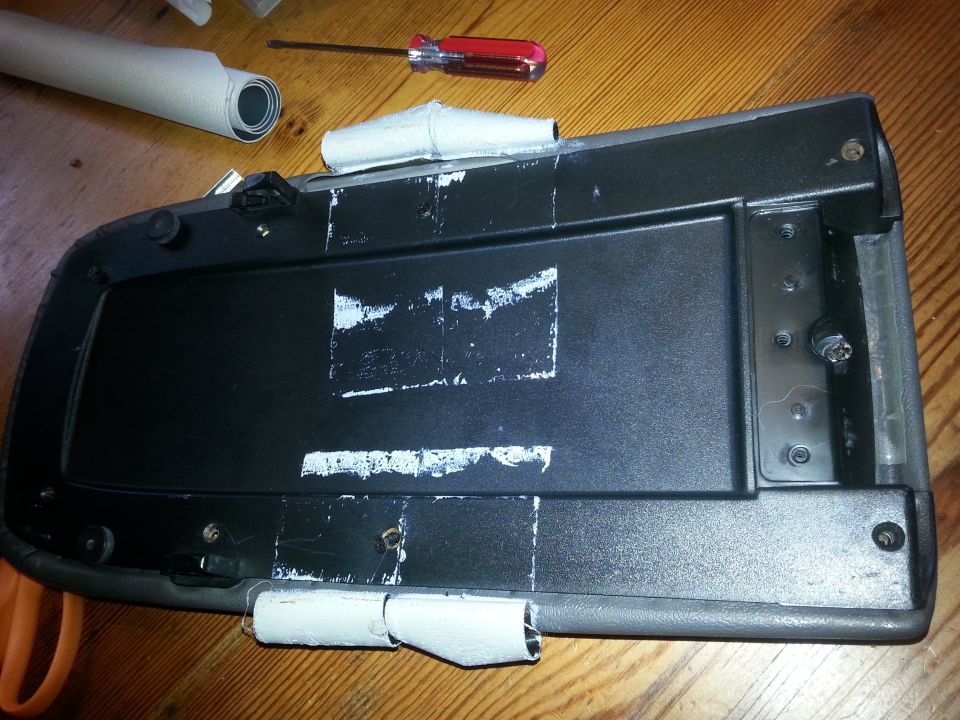 Underside of black center console armrest lid with white tape and screws.