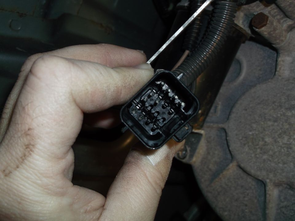 Close-up of a vehicle's electrical connector with pins, held by a hand.