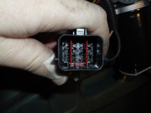 2005 Ford F-150 - A hand with a bandage on a finger holds a black electrical connector with visible pins and red plastic inserts. The connector is attached t…