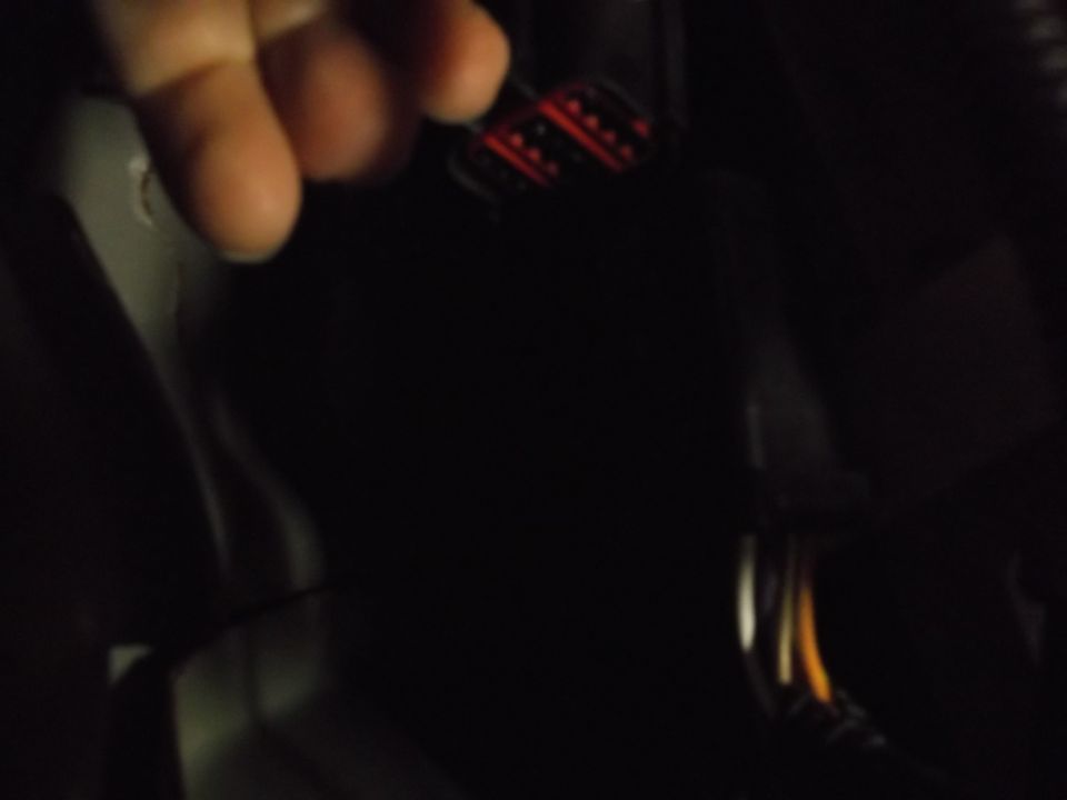 Dark interior closeup of a hand near a red and black electrical connector