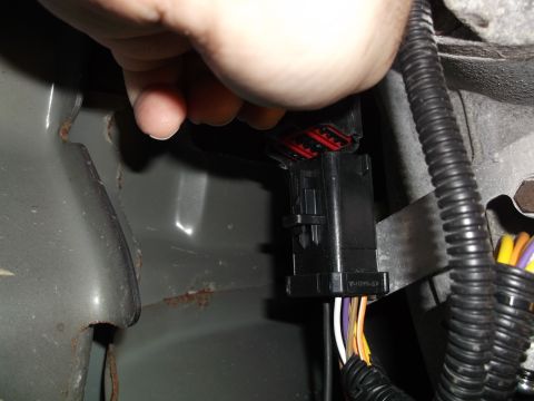 2005 Ford F-150 - A hand is shown disconnecting a black electrical connector with red terminals from a vehicle harness. The connector is attached to a bundle…