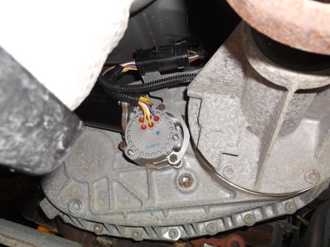 2005 Ford F-150 - A close-up, low-angle view of a vehicle's transfer case with a sensor attached. The transfer case is made of gray metal and has various bol…