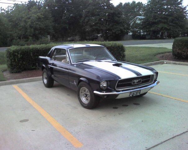 1967 Ford Mustang coupe, dark blue with white racing stripes, parked in a lot.