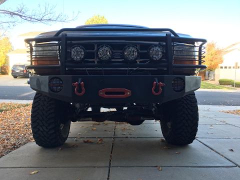 1996 Ford Bronco - Front view of a modified dark-colored SUV, likely a Ford Bronco, with a heavy-duty bumper, winch, and multiple KC lights mounted on a brush…
