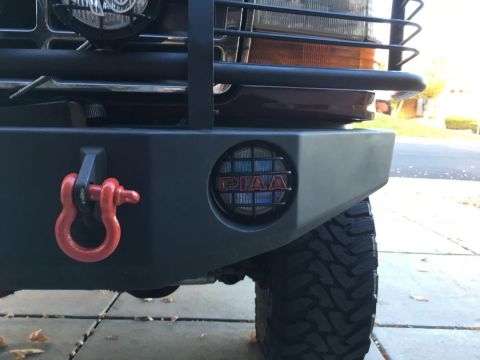 1996 Ford Bronco - Close-up of the front bumper of a dark red vehicle, featuring a red tow shackle and a PIAA light with a protective grille. The vehicle has…