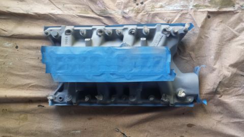 1996 Ford Bronco - A gray intake manifold, partially covered with blue painter's tape, sits on a brown drop cloth.