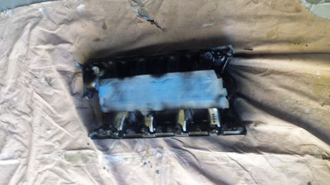 1996 Ford Bronco - A black intake manifold is shown partially covered with blue painter's tape, resting on a brown drop cloth. The manifold appears to be a ve…