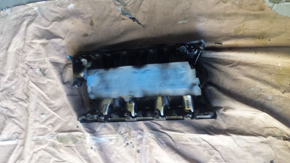 Black intake manifold with blue tape on a brown drop cloth.