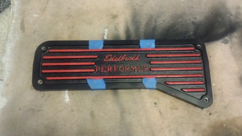 1996 Ford Bronco - A black Edelbrock Performer valve cover with red accents and lettering is shown, secured with blue painter's tape. The part is laying on a…