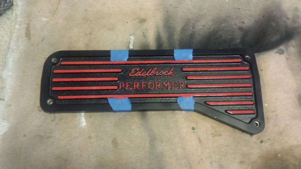 Black Edelbrock Performer valve cover with red stripes and lettering, taped down.