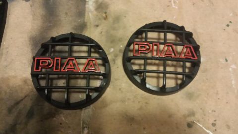 1996 Ford Bronco - Two black grilles with red "PIAA" lettering are shown on a textured surface. The grilles appear to be for headlights or driving lights.