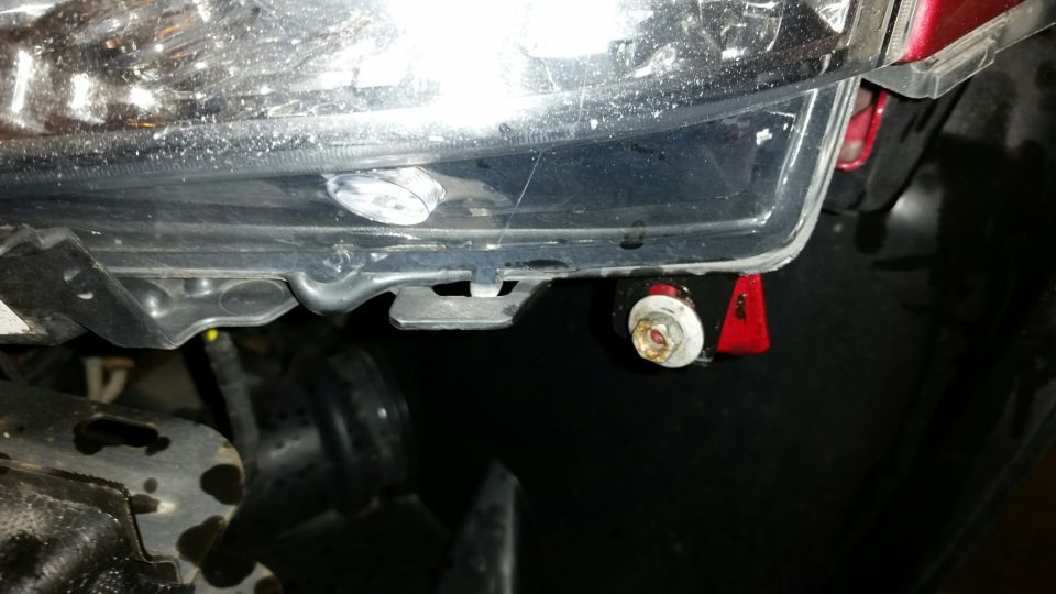 Close-up of a car headlight assembly with a red bracket and bolt.