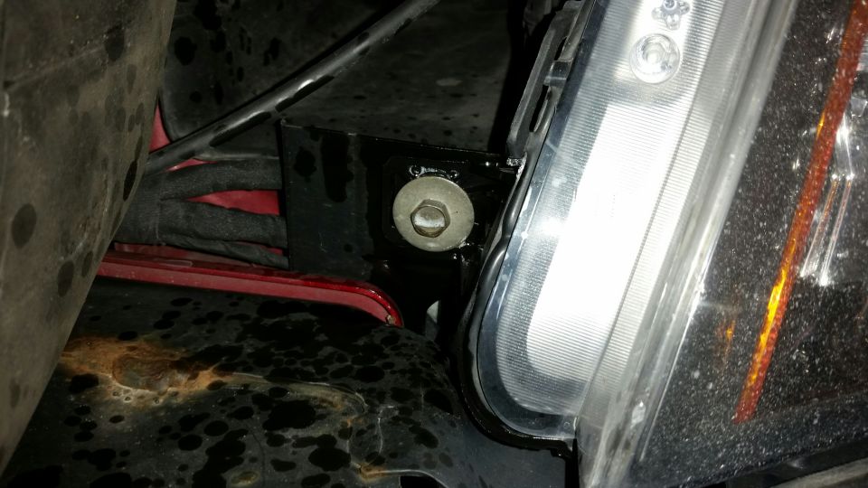 Vehicle headlight assembly with a bolt on a black bracket, red bodywork, and rusted metal.