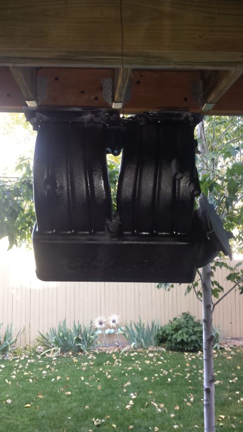 1996 Ford Bronco - A black Edelbrock intake manifold is mounted upside down under a wooden deck, with a backyard scene visible in the background.