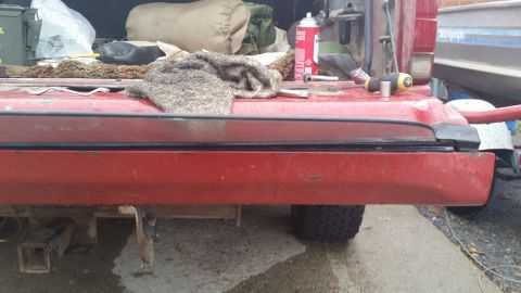 1981 Ford Bronco - The rear of a red pickup truck bed is shown with various tools and items in the bed. A trailer hitch is visible underneath the truck.