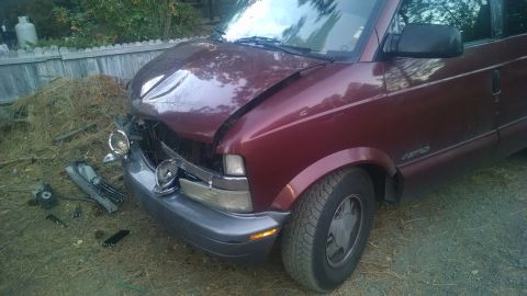 2000 Chevrolet Astro - A damaged maroon Chevrolet Astro van is parked outdoors with its hood crumpled and front bumper dislodged. Debris from the front end is sca…