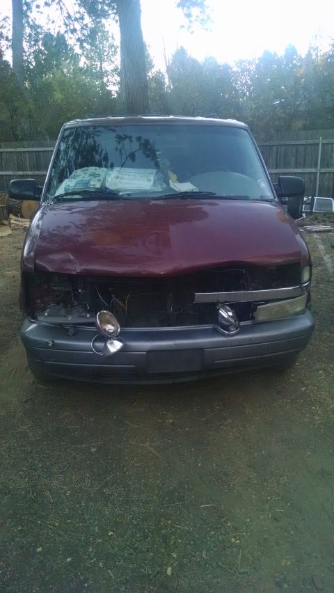 2000 Chevrolet Astro - Front view of a dark red Chevrolet Astro van with collision damage, missing headlight and bent hood, parked in a fenced dirt yard.