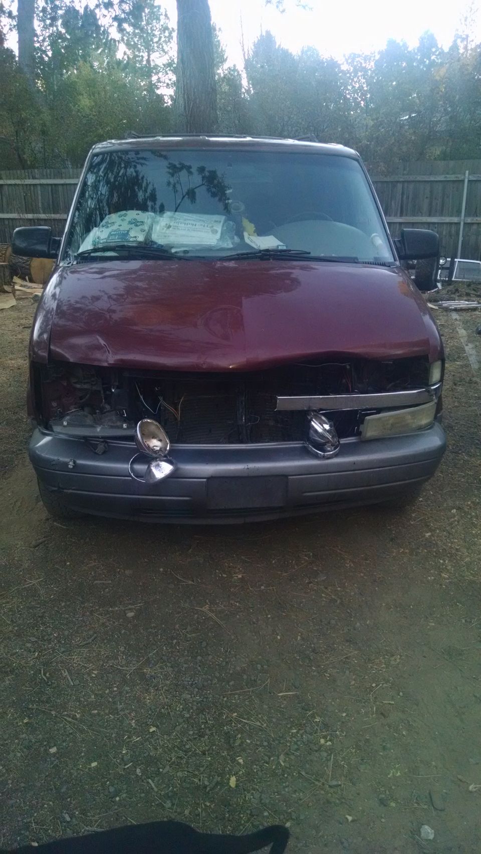 Damaged maroon van front end with dented hood and missing headlights.