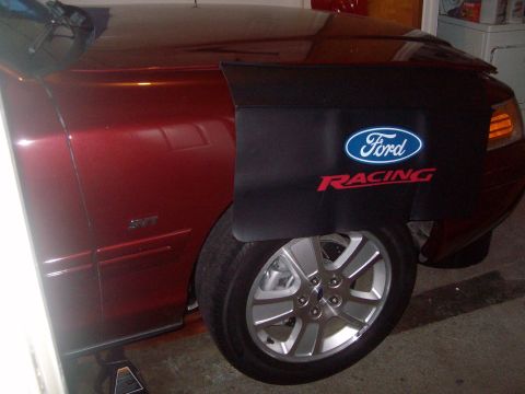 2004 Ford Crown Victoria - A close-up, low-angle shot of the front fender and wheel of a dark red Ford Crown Victoria. A black fender cover with Ford Racing branding…