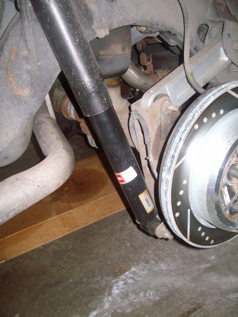 2004 Ford Crown Victoria - A close-up view of the rear suspension components of a dark-colored vehicle, showing a black shock absorber, exhaust pipe, and a slotted br…