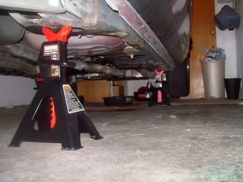 2004 Ford Crown Victoria - A black Craftsman jack stand is supporting the frame of a vehicle, likely a 2004 Ford Crown Victoria, in a garage setting. The vehicle's un…