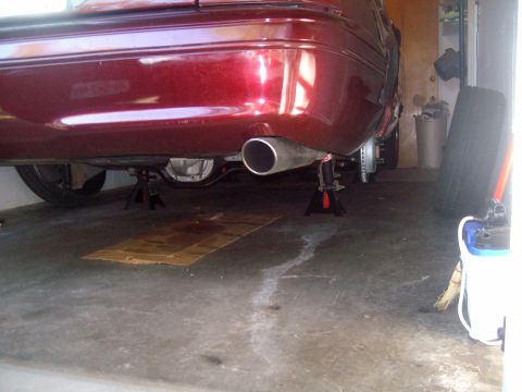 2004 Ford Crown Victoria - The rear underside of a dark red sedan is raised on jack stands in a garage. The car's exhaust pipe, differential, and rear brake rotors ar…
