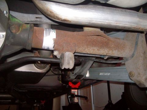 2004 Ford Crown Victoria - The underside of a vehicle shows a rusty driveshaft with a white label attached, connected to the rear differential. A black sway bar with…