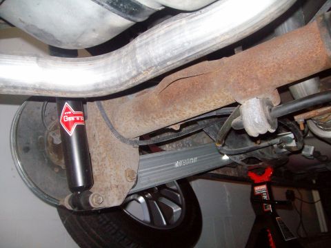 2004 Ford Crown Victoria - The underside of a vehicle shows a rusty rear axle assembly with a KYB "Gas-a-just" shock absorber and a silver aftermarket control arm. A…
