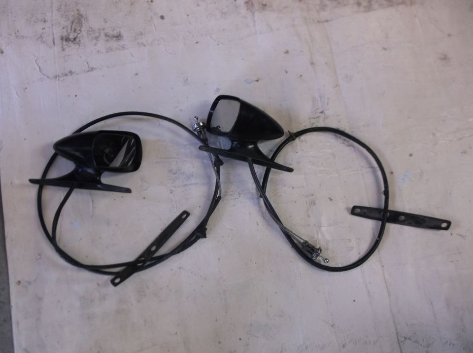 Two black side mirrors with cables and a mounting bracket on a textured surface.