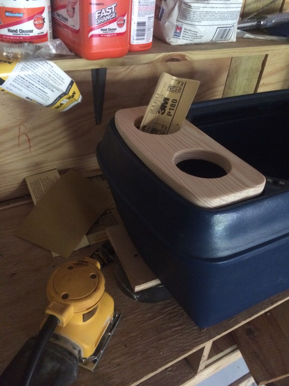 Wooden console top insert with two cutouts on a blue plastic console, with sander and sandpaper nearby