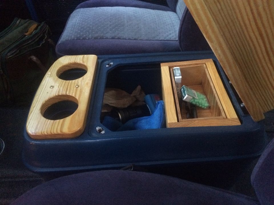 Vehicle interior center console with dual wooden cup holders and a storage compartment containing a flashlight and a small box of mints