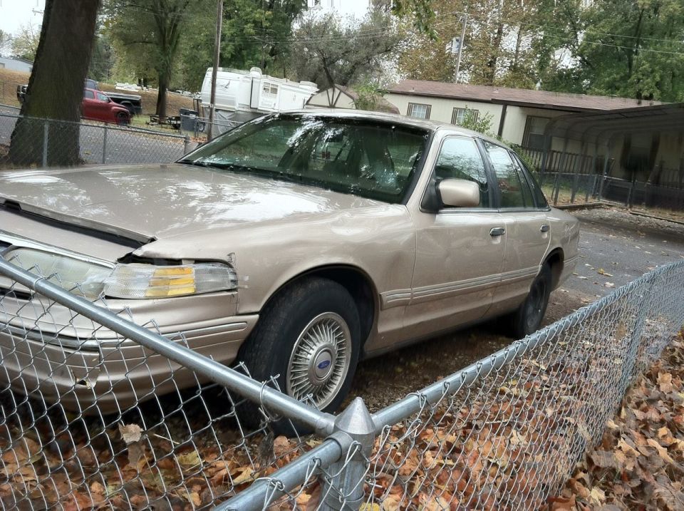 Tan Ford Crown Victoria behind a chain-link fence